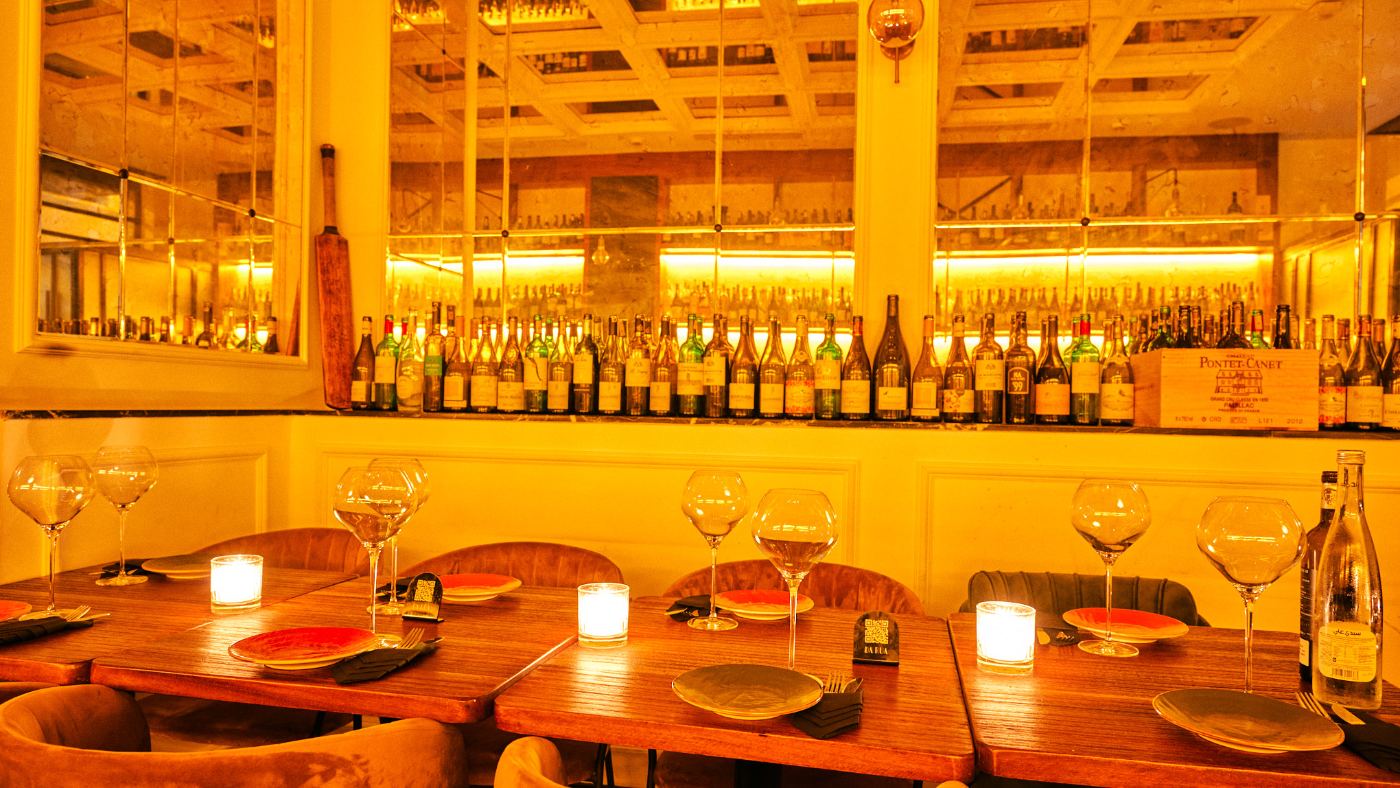 Tables dressées devant le mur de bouteilles, grands verres à vin